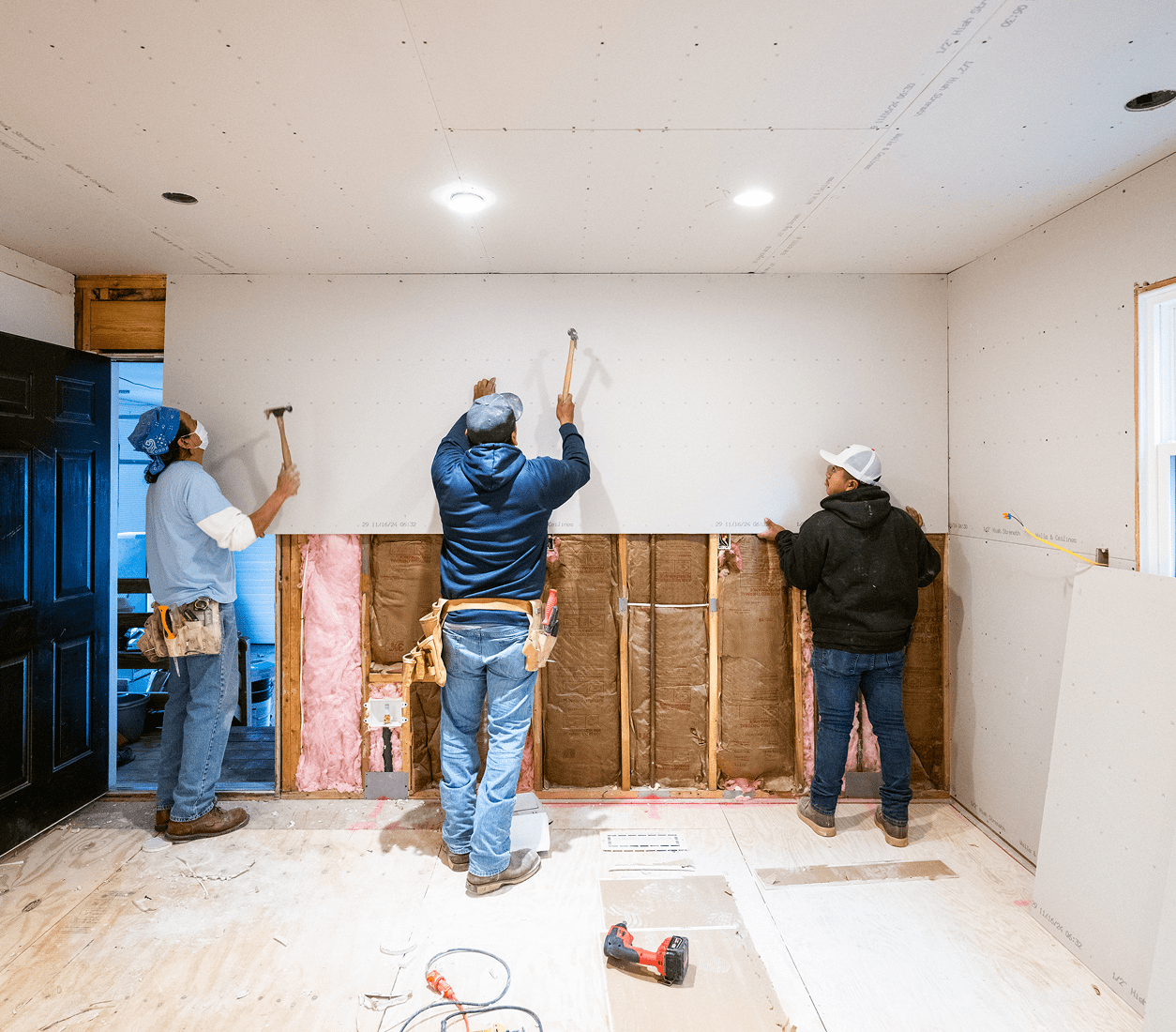Workers hammering drywall panels on wall.